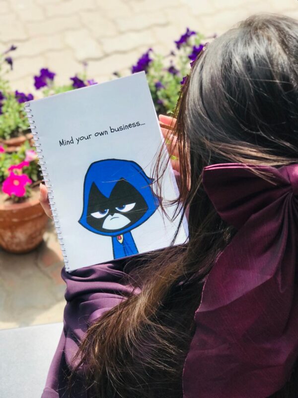 A white spiral-bound notebook featuring a cartoon illustration of Raven from Teen Titans Go! with the text "Mind your own business...." written above her.