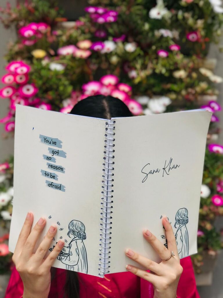 A minimal white spiral notebook featuring a hand-drawn girl illustration and a blue taped-style quote that reads "You've got no reason to be afraid."