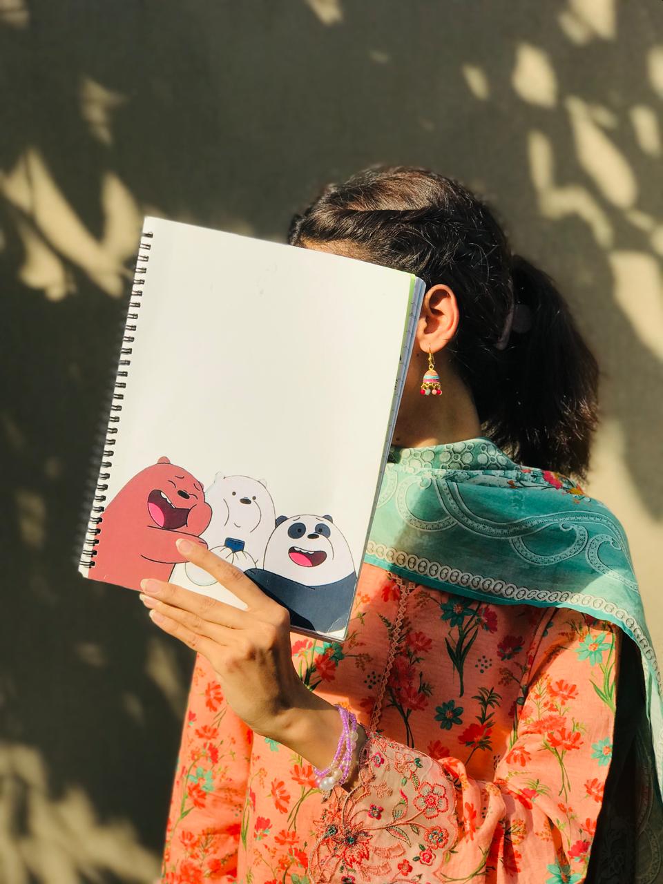 A clean white spiral notebook featuring Grizz, Ice Bear, and Panda from We Bare Bears laughing and posing together at the bottom left corner.
